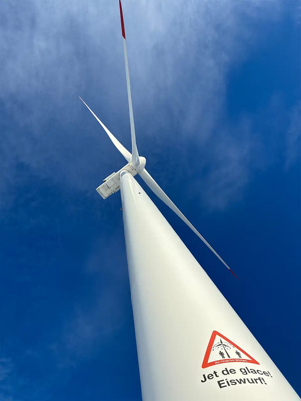 Éolienne vue d'en bas, pales et mât contre le ciel bleu